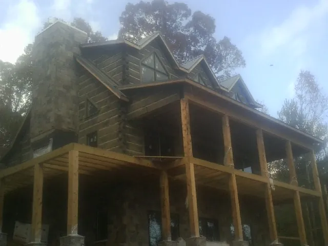 Stone chimney and dormers on a large log home with a timber porch in Plainfield